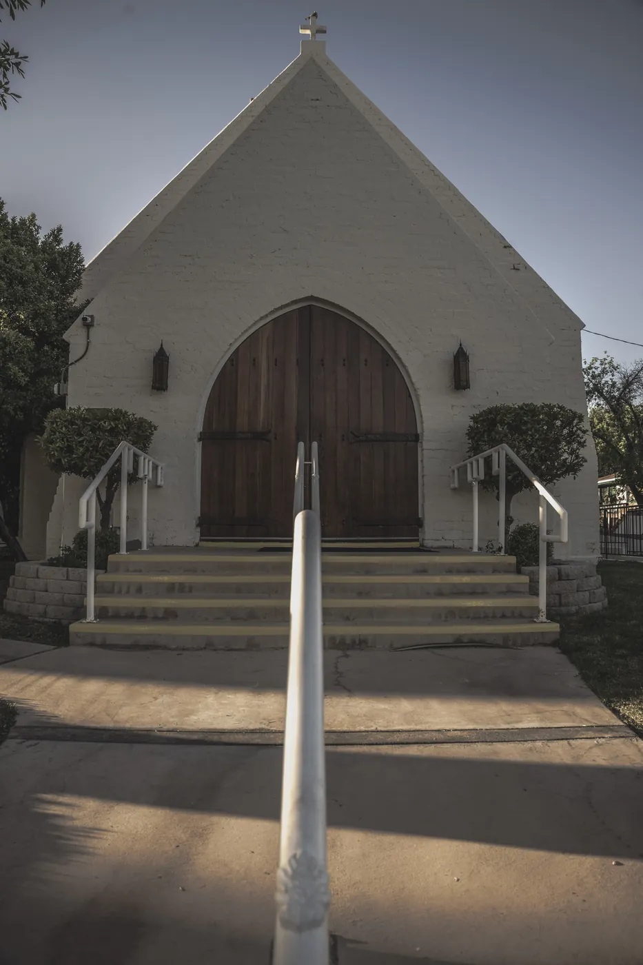 Small white chapel with arched wooden doors and a handrail leading up the steps