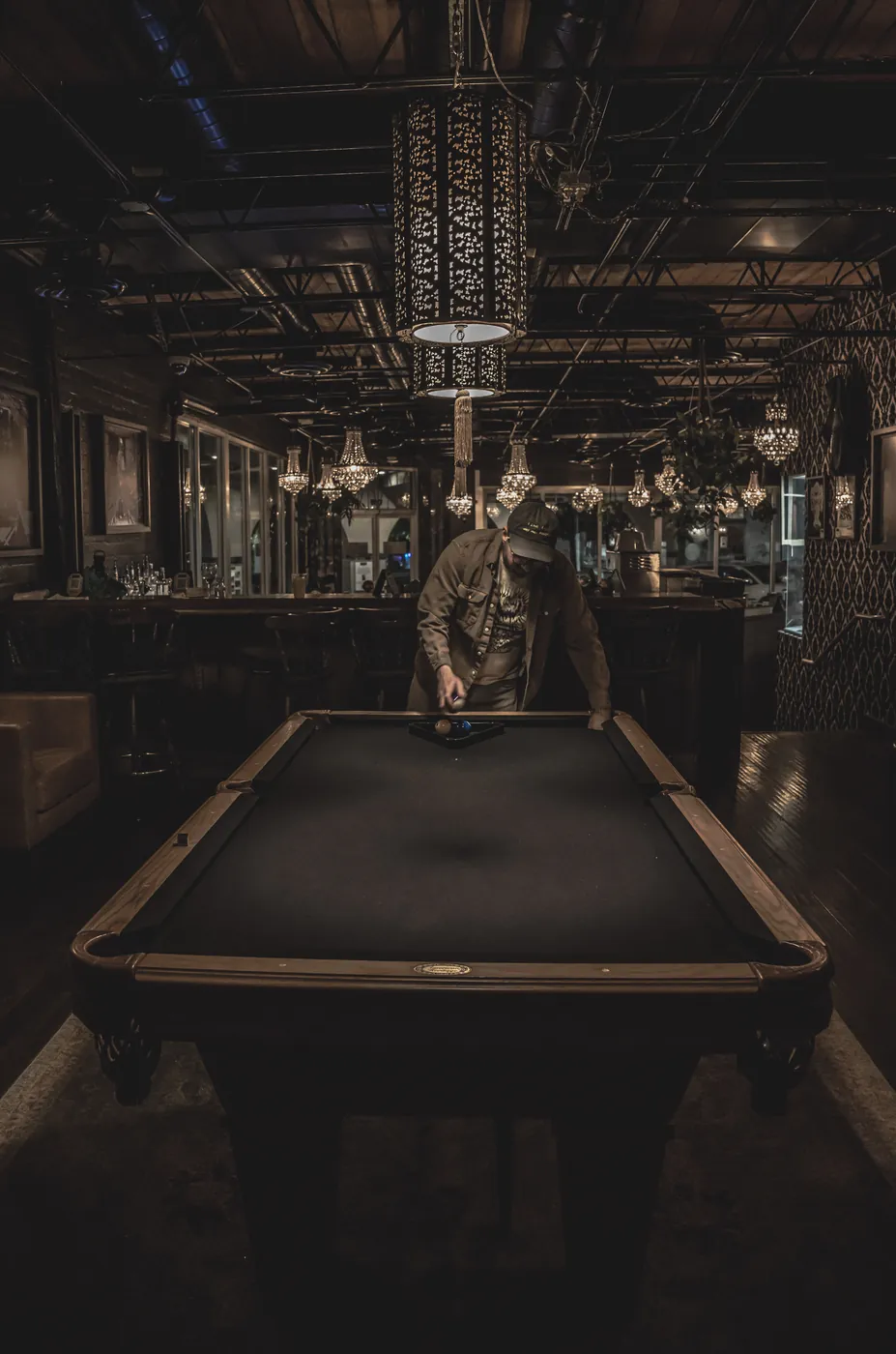 Lone pool player at a table in a dark ornate billiard hall